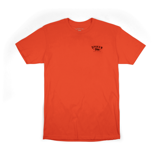 Tee from the front: orange tee with black Spoken Moto flag logo on the upper left chest.