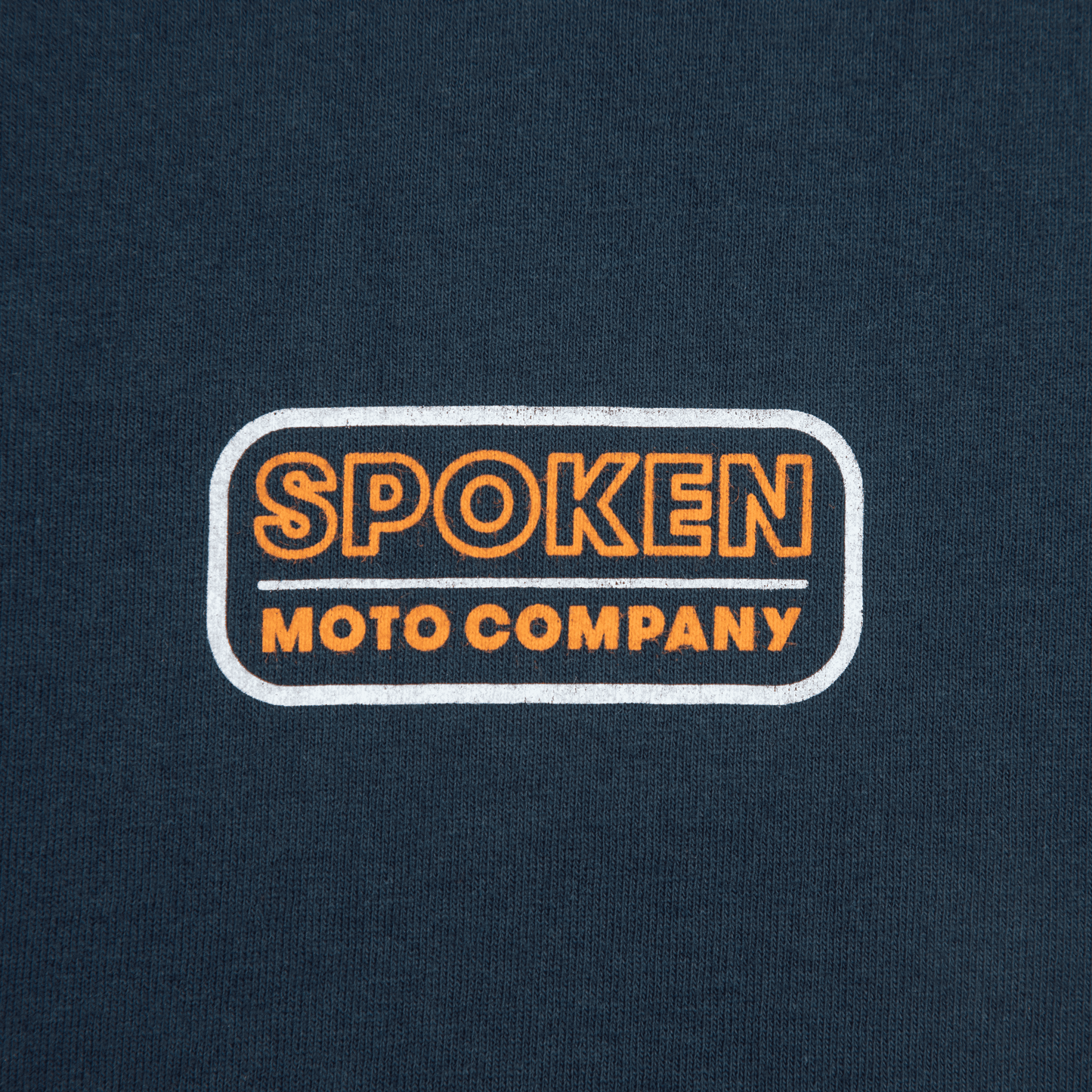 Close up of the orange and white retro Spoken Moto logo on the upper left chest.