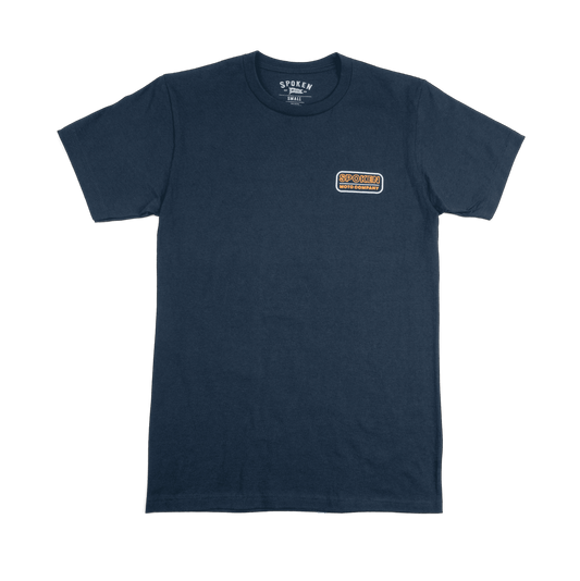 The front of the tee: a navy blue tee with orange and white retro Spoken Moto logo on the upper left chest.