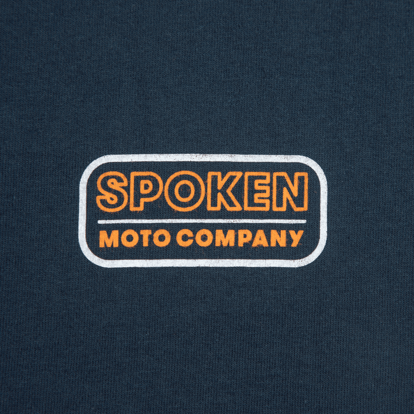 Close up of the orange and white retro Spoken Moto logo on the upper left chest.